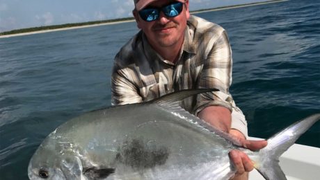 A photo of a man in a pair of sunglasses and a cap holds up a saltwater fish.