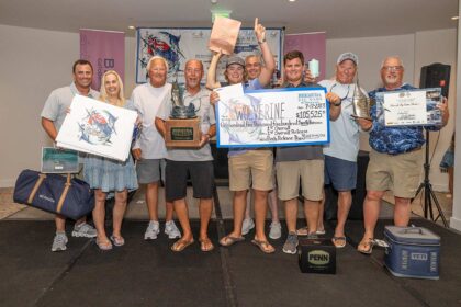 Team Wolverine standing at an awards ceremony holding their prized check, trophies and other awards.