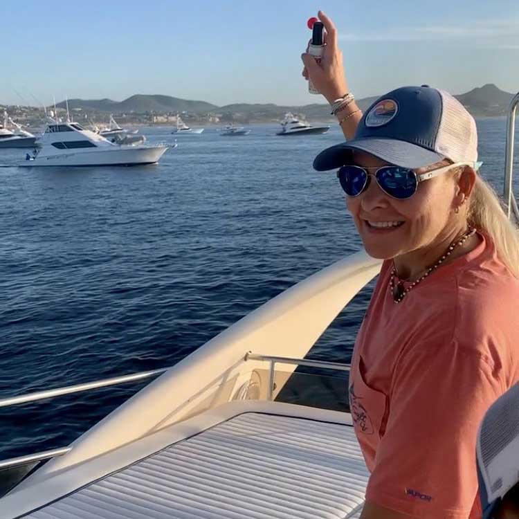 A woman in sunglasses and cap overlooks a bay fillwed with sportfishing boats.