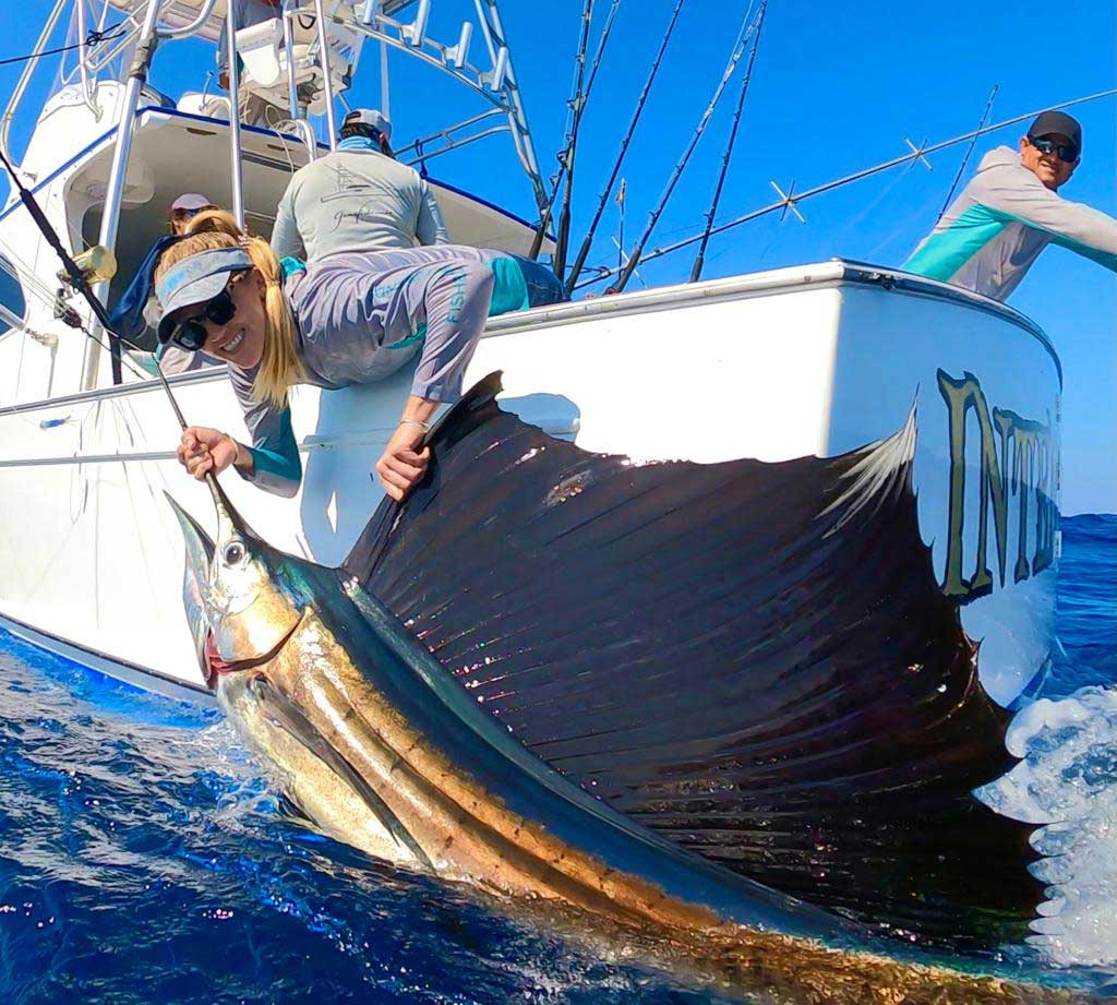 A woman pulls a large sailfish boatside.